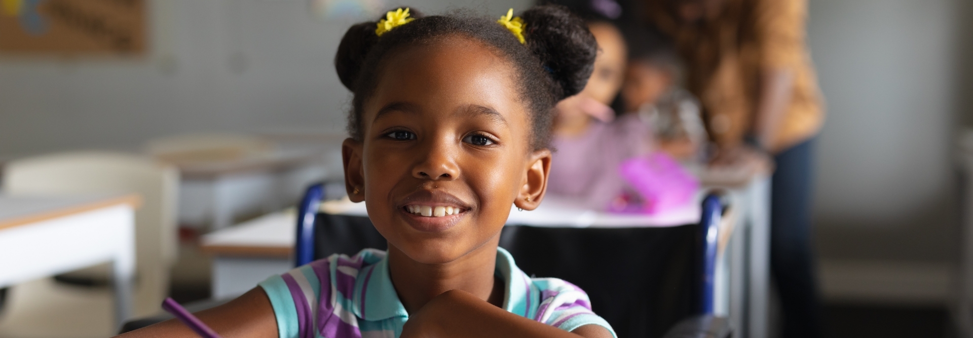 Portrait of smiling african american elementary girl studying while sitting on wheelchair at desk